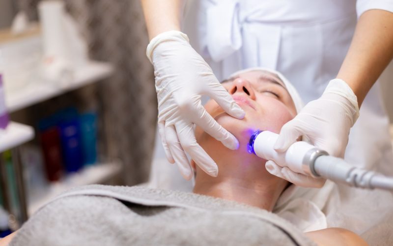 A young beautiful girl lies on the beautician's table and receives procedures with a professional apparatus for skin rejuvenation and moisturizing