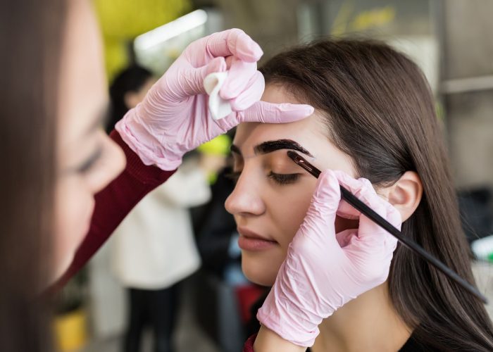Master in white gloves work at eyebrows in beauty salon