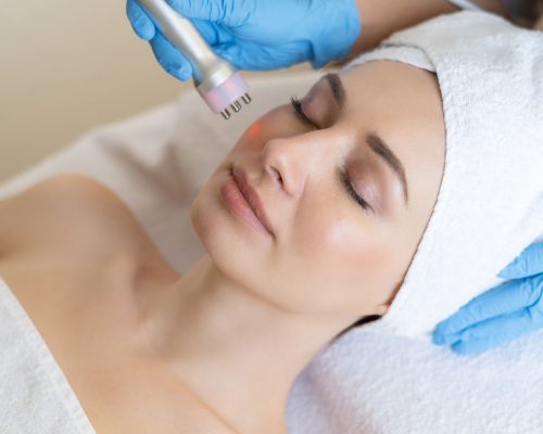 Young woman lying on cosmetologist's table during rejuvenation procedure. Cosmetologist take care about neck and face skin youthfull and wellness. Hardware face cleaning procedure